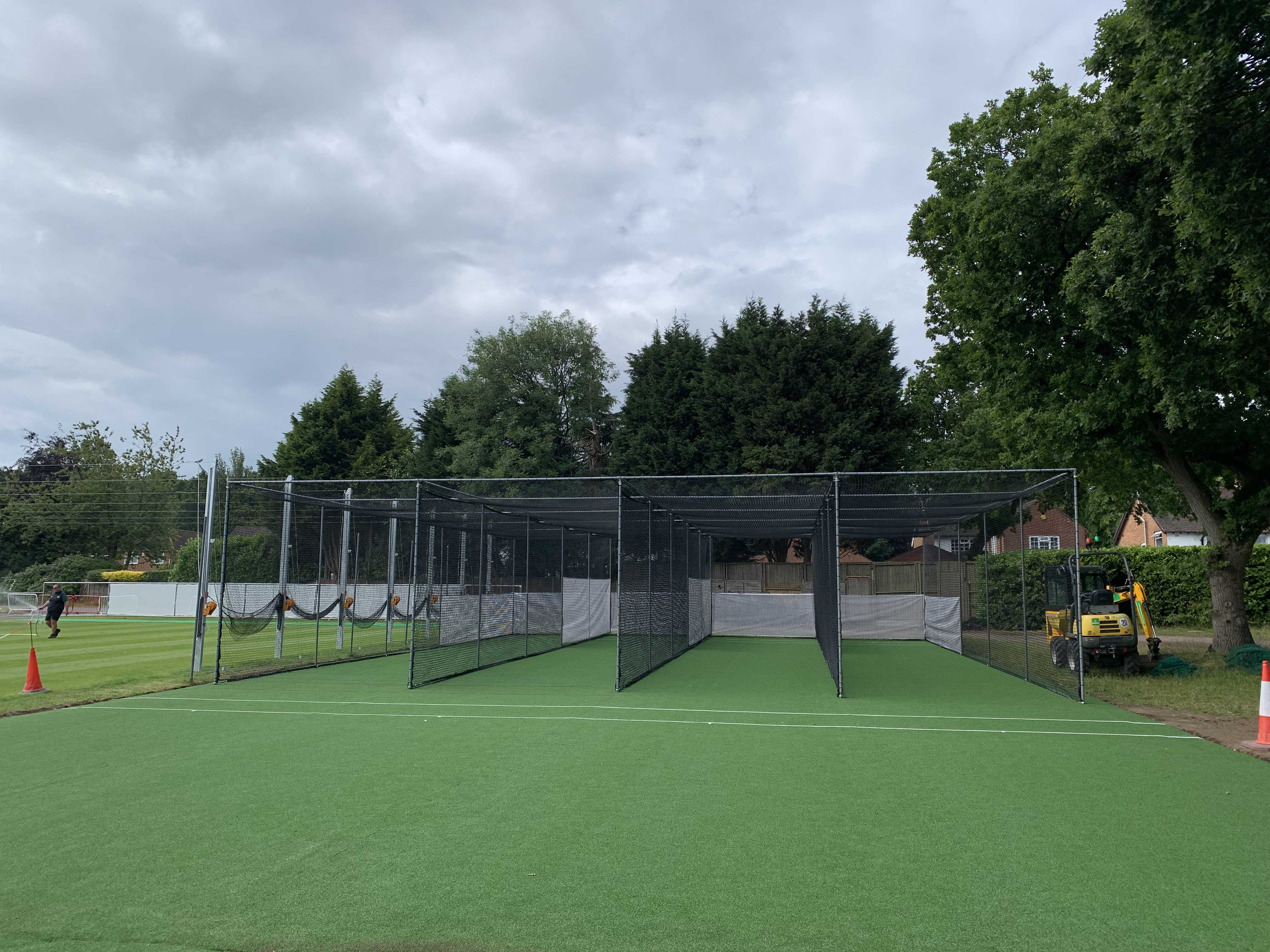 Image shows a four-bay non turf cricket net with black netting and green surfacing
